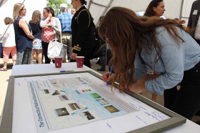 UConn Student Shelby Larubina signs a framed map of the CT NERR after the ceremony. She opened the event with a land acknowledgement statement for the 10 indigenous tribes native to Connecticut.