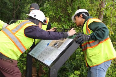 Members of the UConn Sign Services crew use a level to position the Connecticut Blue Trail sign at Bluff Point State Park on June 9.