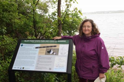 CT Sea Grant Research Coordinator Syma Ebbin stands beside the newly installed CT Blue Heritage Trail sign at Bluff Point on June 9. Ebbin was part of the group that led the project.