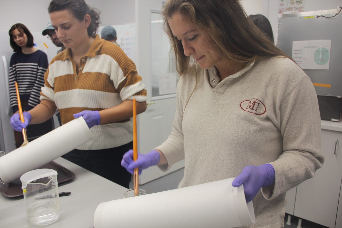 Maggie Aydlett, kelp seed production manager at GreenWave, and Michelle Stephens, hatchery manager, paint a solution containing kelp reproductive tissue onto string wound around a section of PVC pipe.